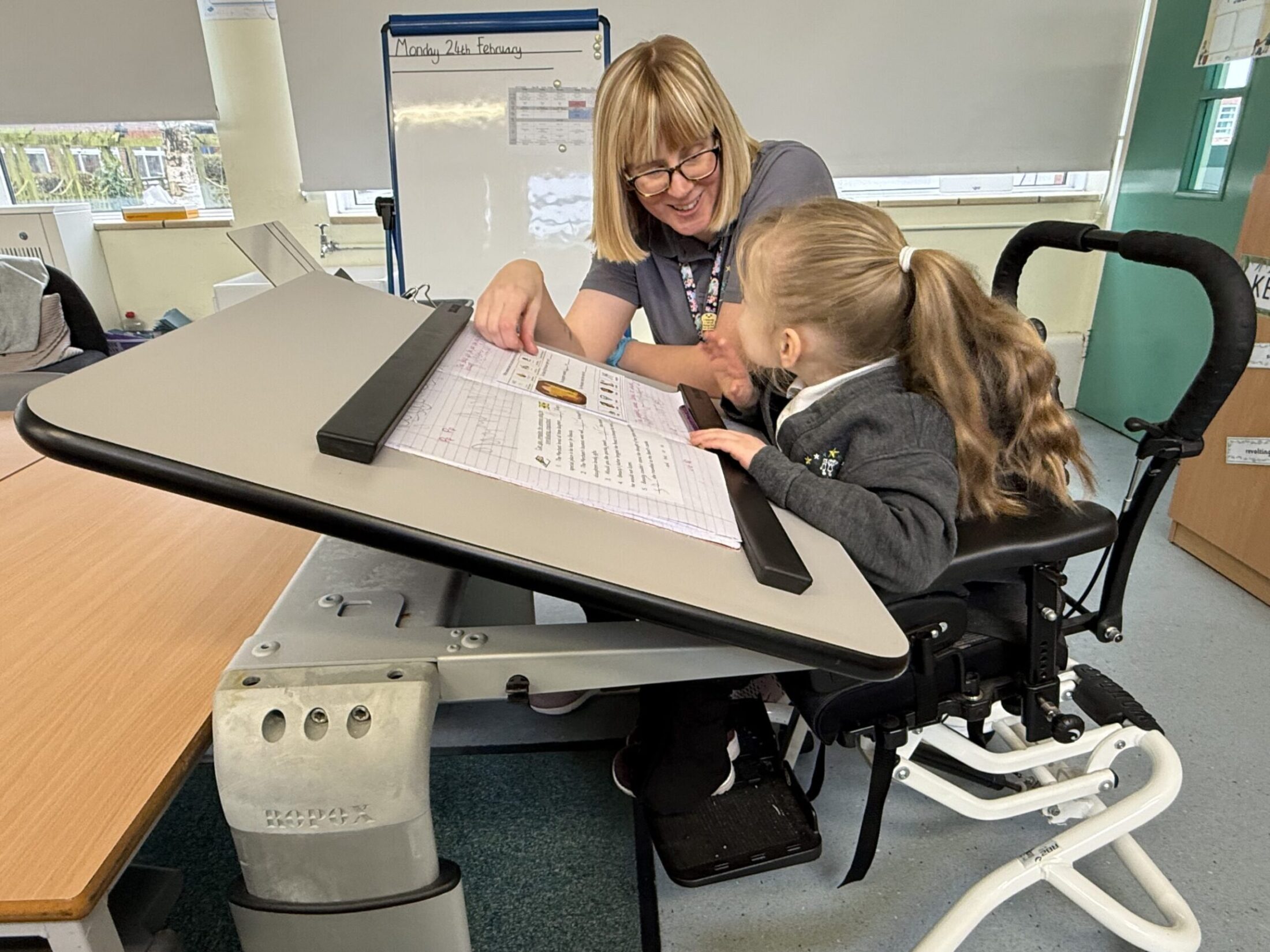 A teaching assistant helps a wheelchair-using girl work at a Ropox Vision Table
